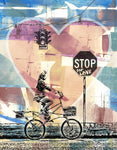 A colorful art print with earthy reds, yellow, green and blues. It has a women cycling on a tall bicyle with and a Stop sign that says, STOP for Love - with a big heart in the background.